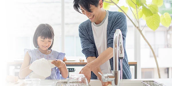 A father washing dishes with his daughter in the kitchen.